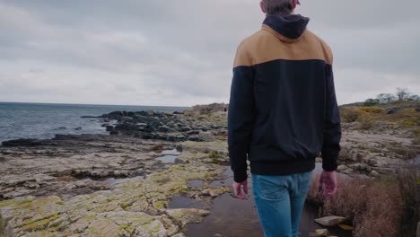 Young-Tall-Guy-With-Cap-Checks-Out-Vårhallarna-Cliffs-and-Keeps-Exploring---Tracking-Wide-To-Medium-Shot