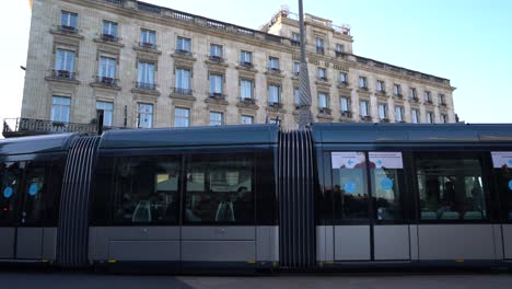 Tramway-car-passes-in-front-of-the-Intercontinental-Hotel-with-people-walking-along,-Handheld-shot