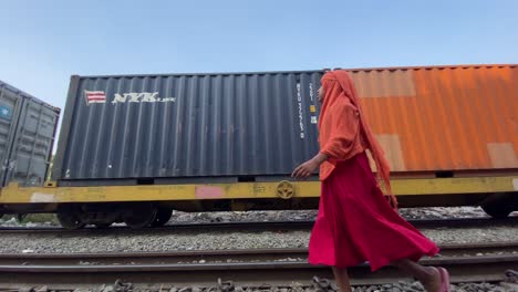 Transporte-De-Contenedores-De-Carga-En-Tren-De-Carga-Pasando-Con-Una-Joven-Musulmana-Caminando