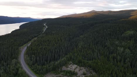 Alpine-road-winding-through-lust-forest-and-mountains-by-Dease-Lake-in-British-Columbia,-Canada-at-sunset