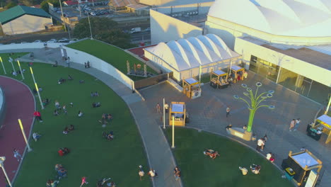 people-enjoying-outdoor-concert,-drone-aerial-video-of-outdoor-terrace,-chill-people-sitting-on-green-synthetic-grass,-chilling,-outside-costa-rica-shopping-mall,-luxury-sunset,-4k