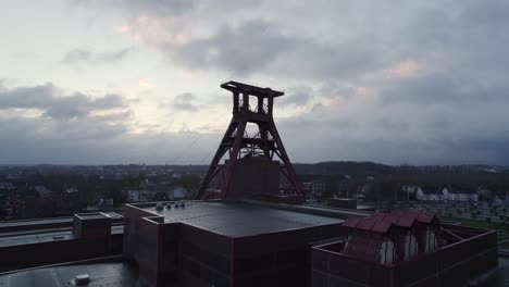 Zeche-Zollverein-Schacht-12-Förderturm,-Hinterleuchtet-Vor-Bewölktem-Morgenhimmel,-Drohne-Zoom-In