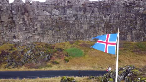 Isländische-Flagge-An-Einem-Windigen-Tag-Im-Thingvellir-nationalpark,-Tourist,-Der-Durch-Den-Thingvellir-nationalpark,-Island-Geht