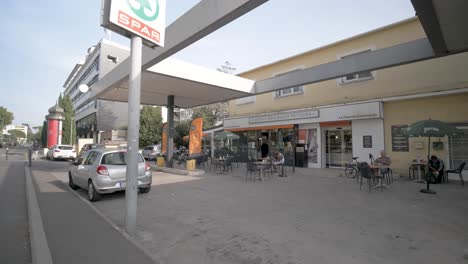 Outside-of-SPAR-Mini-Food-Market-with-people-outside-in-tables-having-lunch,-Pan-right-reveal-shot