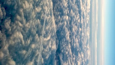 High-angle-pov-of-flying-airplane-above-clouds-leaving-long-white-condensation-vapor-air-trail-in-blue-sky
