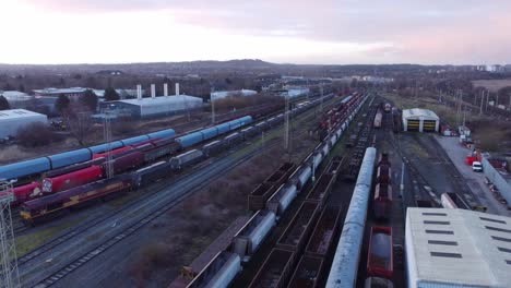 Sunrise-aerial-view-of-long-railroad-tracks-with-heavy-diesel-locomotive-carriages-and-cargo-container-yard-slow-right-orbit