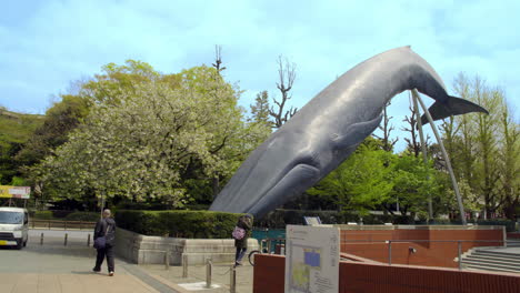 Ueno,-Tokio,-Japón,-Objeto-De-Ballena-Azul-En-El-Museo-Nacional-De-Naturaleza-Y-Ciencia,-Tokio,-Japón-Alrededor-De-Abril-De-2020:-Gente-En-Bicicleta,-Caminando-Frente-Al-Monumento-En-Un-Día-Nublado-De-Primavera