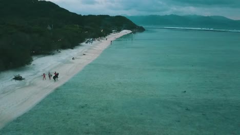 Spectacular-aerial-flight-fly-backwards-drone-shot-of-a-guy-riding-slow-on-a-horse-on-a-white-sand-dream-beach-Gili-Trawangan-Bali-Lombok-a-small-island-at-blue-hour-after-sunset-by-Philipp-Marnitz