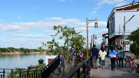 Gente-Que-Pasa-Mientras-Un-Grupo-Va-Al-Frente-Del-Río-Y-Luego-Otros-Pasan-Con-Bicicletas,-Calle-Peatonal,-Chiang-Khan,-Loei-En-Tailandia