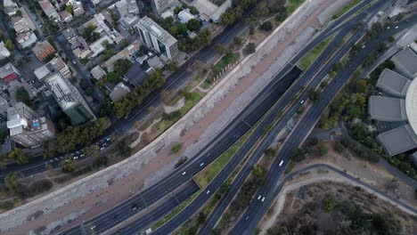 Aerial-top-down-dolly-in-of-Mapocho-river-and-cars-driving-in-avenues-and-highway-and-Santiago-city-neighborhood-buildings,-Chile
