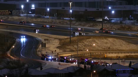 Traffic-Going-Past-On-Highway-With-Row-of-Snow-Plough-Trucks-Queuing-Up-Off-Exit-At-Night