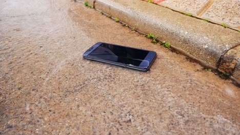 Wasserdichtes-Modernes-Smartphone,-Das-Auf-Der-Straße-Liegt-Und-Vom-Regenabfluss-Nass-Wird