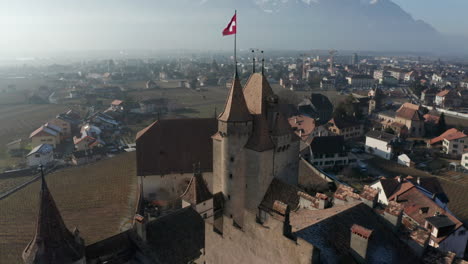 Aerial-of-old-castle-tower-with-a-Swiss-flag-flying-on-top