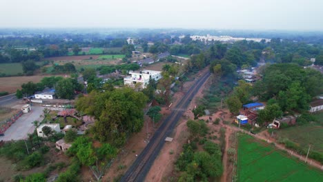 Toma-Aérea-De-Drones-Que-Viaja-Hacia-Arriba-De-Las-Vías-Del-Tren,-Una-Carretera-Y-Campos-De-Cosecha-Alrededor-De-La-Ciudad-De-Gujarat,-Vadodara,-India