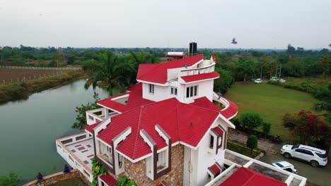 Pájaros-Negros-Volando-En-Bandada,-En-Rotación-A-Una-Lujosa-Casa-De-Vacaciones,-Con-Un-Dron-Aéreo,-Y-Un-Fondo-De-Lago-Y-Palmeras-Con-Una-Sensación-De-Relajación-En-Vadodara,-India