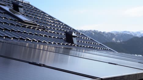 Solar-panel-installation-on-private-home---Moving-slowly-down-along-panels-with-black-shiny-roof-and-snowy-mountains-in-background---Norway-Europe