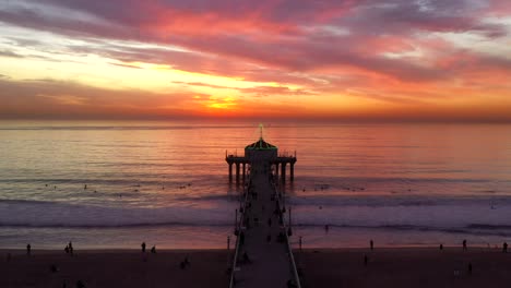 Fiery-Sunset-Sky-In-Manhattan-Beach-Pier-With-People-Swimming-During-Summer-In-California,-United-States
