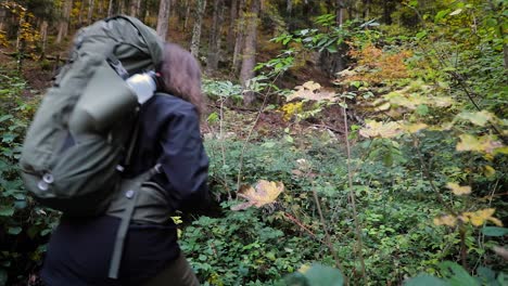 Female-woman-hiker-with-backpack-walking-off-trail-through-overgrown-forest-foliage
