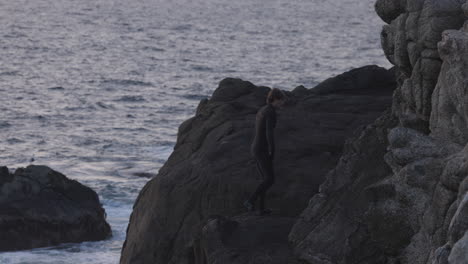 Adult-male-climbs-cliff-and-cliff-jumps-off-into-the-ocean-at-sunset