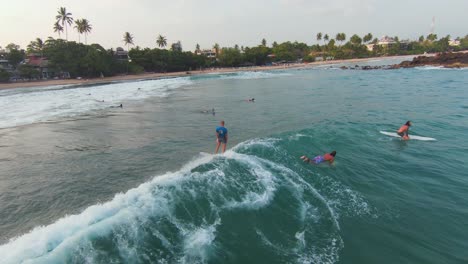 FPV-Tracking-Shot-Of-Team-Surfing-Together-Over-Long-Wave-In-Beautiful-Beach-Island,-Sri-Lanka