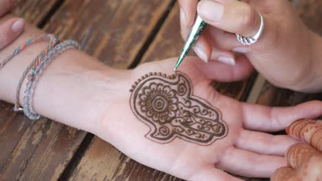 Tatto-artist-putting-a-henna-tatto-on-woman's-handpalm