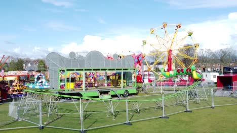 Small-town-fairground-Easter-holidays-funfair-rides-in-public-park-aerial-rising-view