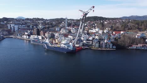 Massive-heavy-lifting-barge-Uglen-from-Ugland-company-alongside-in-Leirvik-Stord-Norway---Upward-moving-aerial-with-tilt-down-and-Leirvik-town-in-background