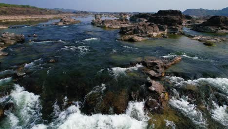 Aerial-forwarding-moving-shot-over-scenic-river-Narmada-in-Gujrat,-India-flowing-through-rocky-terrain-on-a-bright-sunny-daytime