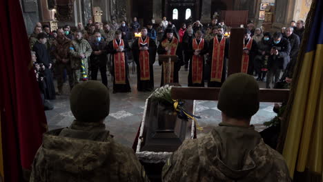 Zwei-Soldaten-Stehen-über-Einem-Geschlossenen-Sarg-Eines-Gefallenen-Kameraden,-Während-Priester-Davor-Stehen-Und-Eine-Zeremonie-Bei-Der-Beerdigung-Eines-Ukrainischen-Soldaten-Während-Der-Russischen-Invasion-Des-Landes-Durchführen