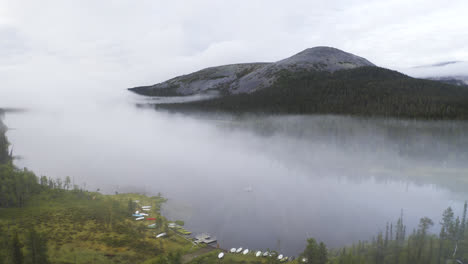 Aerial-view-of-a-lake-filled-with-mist-going-closer-to-a-person-rowing-a-boat