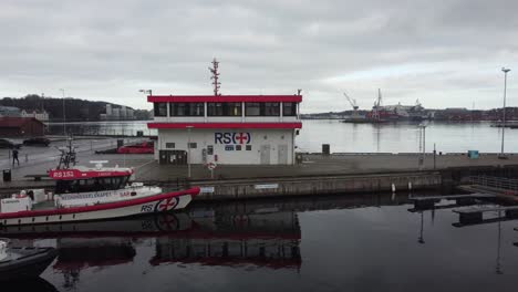 Building-of-sea-rescue-company-Redningsselskapet-in-Stavanger-Norway---Aerial-approaching-building-with-fjord-in-background-and-rescue-boats-in-front