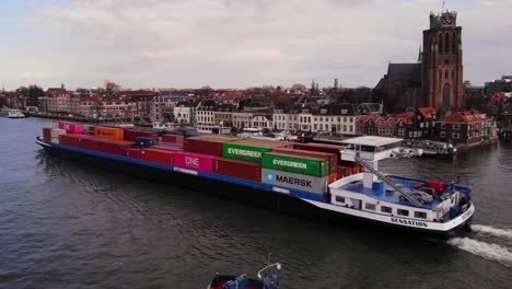 Aerial-Along-Port-Side-View-Of-Sensation-Cargo-Vessel-Going-Past-On-Oude-Maas-With-Our-Lady-of-Dordrecht-In-Background