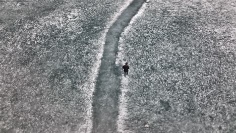 Aerial-Birds-Eye-View-Of-Adult-Male-Walking-Across-Snow-Covered-Ground-At-Khalti-Lake
