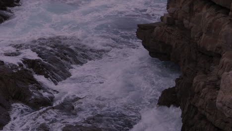 Close-up-of-waves-crashing-on-to-coastal-rocks-and-then-retreating