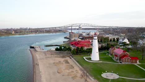 Fort-Gratiot-Lighthouse-in-Port-Huron,-Michigan-with-Blue-Water-Bridge-in-background-drone-video-moving-forward