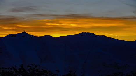 Time-lapse-shot-of-sun-coloring-sky-in-orange-and-golden-colors-behind-mountain-range-silhouette