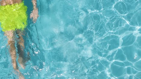 Topdown-view-of-Boy-in-yellow-trunks-swims-along-Translucent-water-on-Swimming-pool