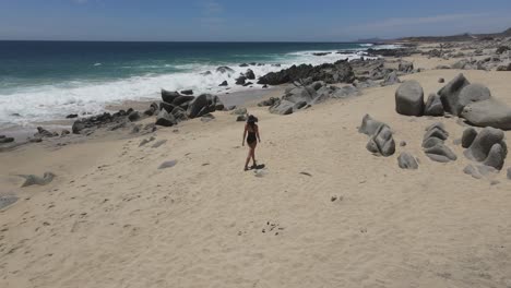 Skinny-girl-walking-in-a-black-swim-suit-with-a-black-hat-on-a-rocky-beach-in-South-California