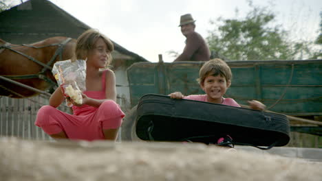 SUPER-CUTE-kids-smiling-on-the-street-in-rural-Romania,-one-with-a-guitar-case
