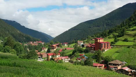 aerial-drone-flying-over-a-hill-revealing-a-mountain-village-during-a-summer-morning-in-Uzungol-Trabzon-Turkey-surrounded-by-a-mountainous-forest-and-hotels