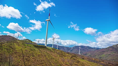 Time-lapse-shot-of-rotating-wind-turbine-farm-located-on-hills-during-sunny-day-with-flying-clouds-at-sky