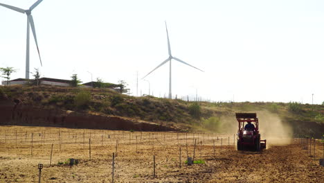 Tractor-Agrícola-Arando-Y-Preparando-La-Tierra-Para-Sembrar-Con-Turbina-Eólica-De-Molino-De-Viento-En-El-Fondo,-Concepto-Ecológico-Sostenible-Verde