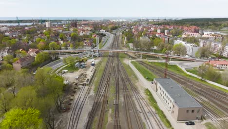 Vista-Aérea,-Puente-Peatonal-Que-Pasa-Por-La-Concurrida-Calle-De-Coches-Y-Las-Vías-Del-Tren