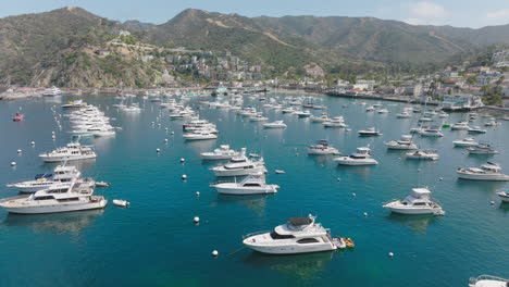 Toma-Aérea-Acercándose-A-Los-Barcos-Anclados-En-El-Agua-Brillante-Del-Océano,-Perspectiva-De-Drones-De-Los-Barcos-En-El-Puerto-Azul-Turquesa-En-La-Isla-Catalina