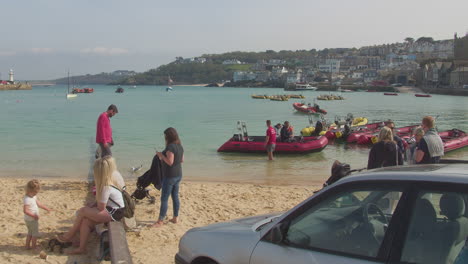 Espera-Turística-Mientras-La-Gente-Regresa-Del-Viaje-En-Lancha-Rápida-En-La-Orilla-Arenosa,-Puerto-De-St-Ives,-Cornualles,-Inglaterra,-Reino-Unido