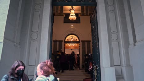 Handheld-tilt-up-of-the-entrance-to-the-Bruna-Palace,-group-of-people-taking-a-tour-on-heritage-day,-Santiago,-Chile