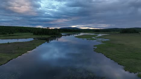Blue-hour-aerial-flying-over-river-floodplain-reflection-clouds