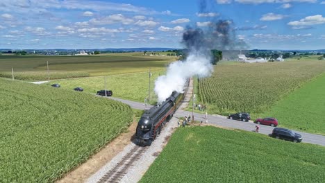 Eine-Luftaufnahme-Eines-Antiken-Dampfpersonenzuges,-Der-Rauch-Und-Dampf-Bläst,-Der-An-Einem-Schönen-Sonnigen-Sommertag-Durch-Fruchtbare-Maisfelder-Fährt