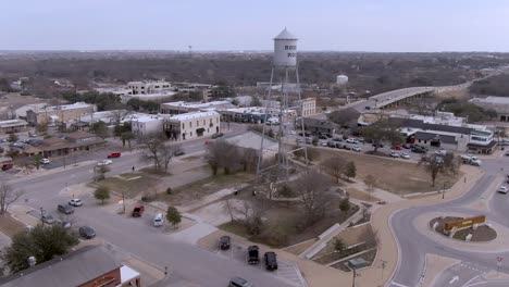 Aerial-pan-up-reveal-and-fly-by-of-silver-water-tower-in-downtown-Round-Rock,-Texas