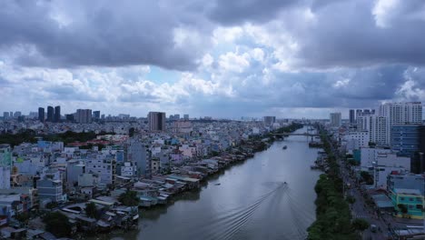 Aerial-view-along-an-urban-canal-in-Saigon-or-Ho-Chi-Minh-City,-Vietnam-with-dramatic-sky-and-boats-in-wet-season
